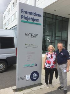 A man and woman stand next to a large sign with Danish writing. 
