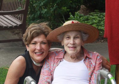 A younger woman has her arm around an old woman in a chair.