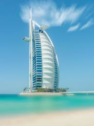 A skyscraper that resembles a huge sail is located in Dubai, surrounded by water.
