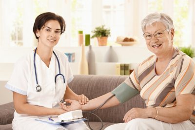 A female nurse wearing a stethoscope take the pulse and blood pressure of an older woman.