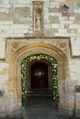A grand, stone front entrance is draped in flowers and boughs.