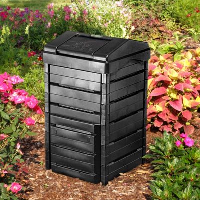 A black plastic compost bin sits among plants and flowers.