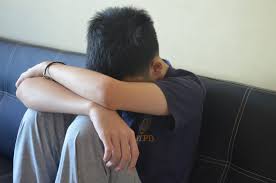 A boy sits with his head dead resting on his forearms.