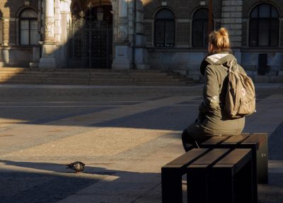 A girl with brown hair up sits alone on a bench with her back to the camera.