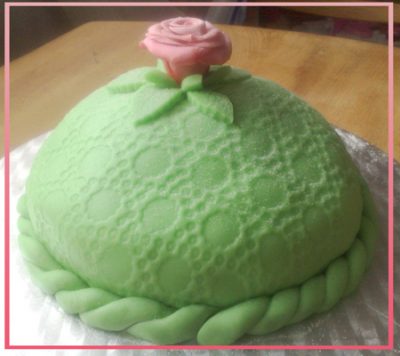 A round, mint green cake with a frosting rose sits on a table.