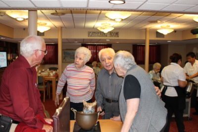 Four older adults talk to one another in a room with tables called "Gathering Room."