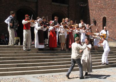 Several people dance and play violins on outdoor steps.