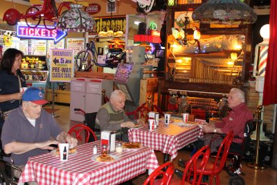 Old men eat pizza at checkered-clothed tables surrounded by paraphernalia and memorabilia in the Volo Museum.
