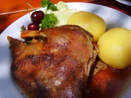 A roasted duck with skin on sits on a plate alongside potatoes and fruit garnish.