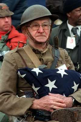 A uniformed veteran of WWI holds an American flag folded in military style.