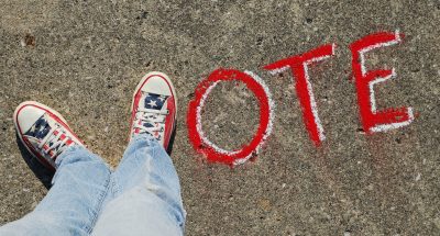 A pair of red, white and blue shoes with stars provides the "V" in a chalk-written word "VOTE" on a sidewalk.