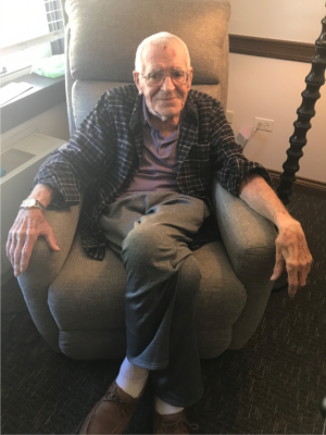An elderly man sits in a chair.