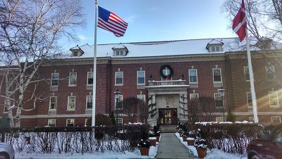 A large, snow-covered mansion fronted by American and Danish flags is decorated for Christmas.