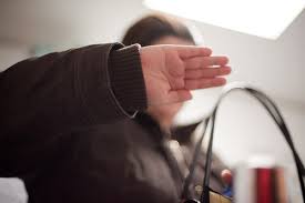 A woman hides her face from the camera with her hand.