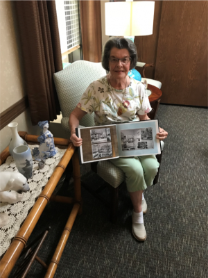 An older woman seated in a chair poses with a photo book.