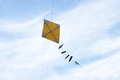 A yellow kite flies in a blue sky.