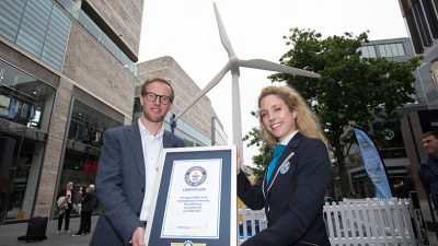 A man and a woman hold a Guinness World Record award for the largest LEGO brick wind turbine.