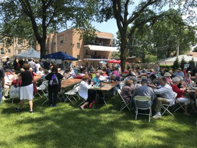 People sit outside eating at picnic tables on a sunny lawn.