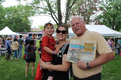 An older man and a woman with a child in her arms pose at an outdoor festival.