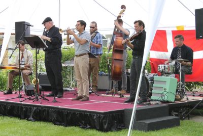 A group of musicians play outside on a stage with a Danish flag in the background.