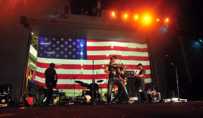 Country singers perform with a huge American flag in the background.