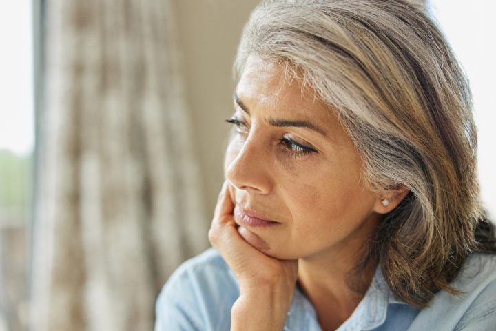 Head And Shoulders Shot Of Thoughtful Mature Woman Looking Out Of Window At Home